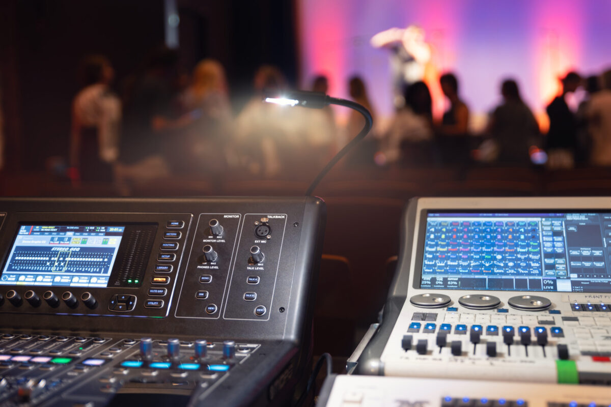 Live theater concert show sound video music control console with scene lights background. Sound engineer mixer soundboard equipment with many knobs, buttons, faders, equalizer screen and light